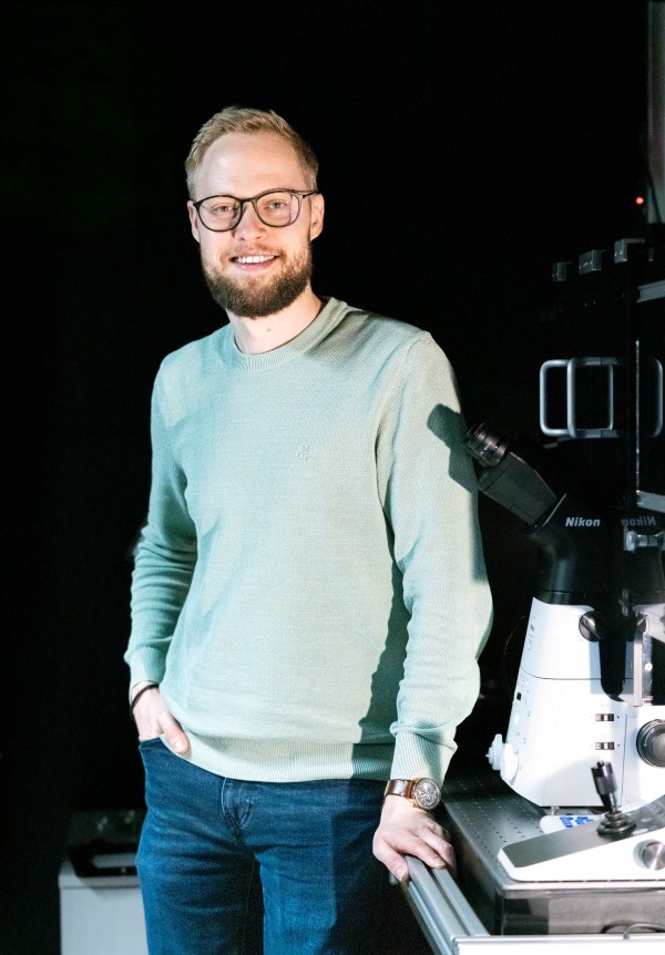 Erstautor der Studie Benjamin Springstein neben einem Mikroskop.